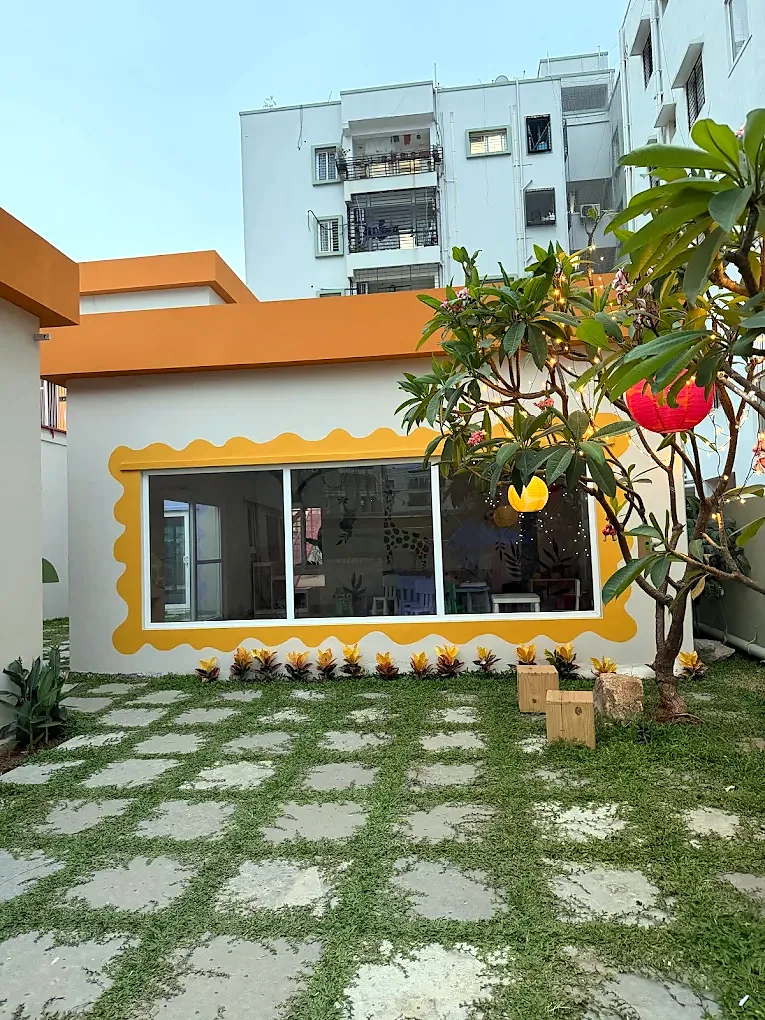 The garden house at Five Little Tales, with a wavy yellow window frame, frangipani tree and stepping-stone lawn